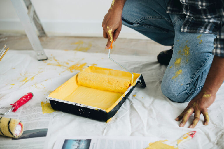 Person kneeling, rolling yellow paint onto a roller over a drop cloth.