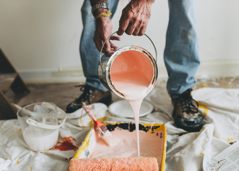 Person pouring pink paint from a can into a roller tray on the floor.