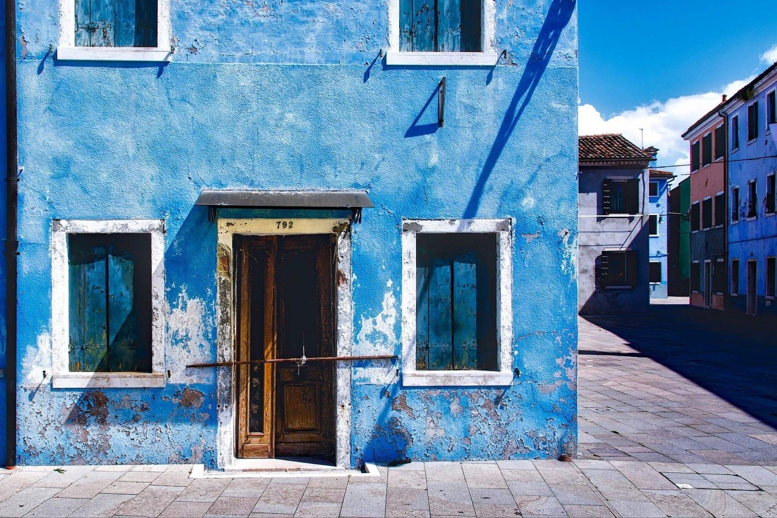 A blue house featuring a door and windows, showing recent plaster repair work on its exterior.