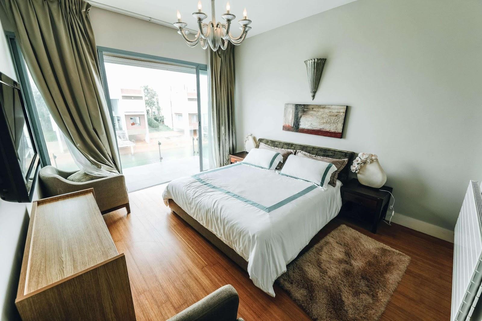 A cozy bedroom featuring a bed, television, and chandelier, adorned with eco-friendly paint for a sustainable touch.