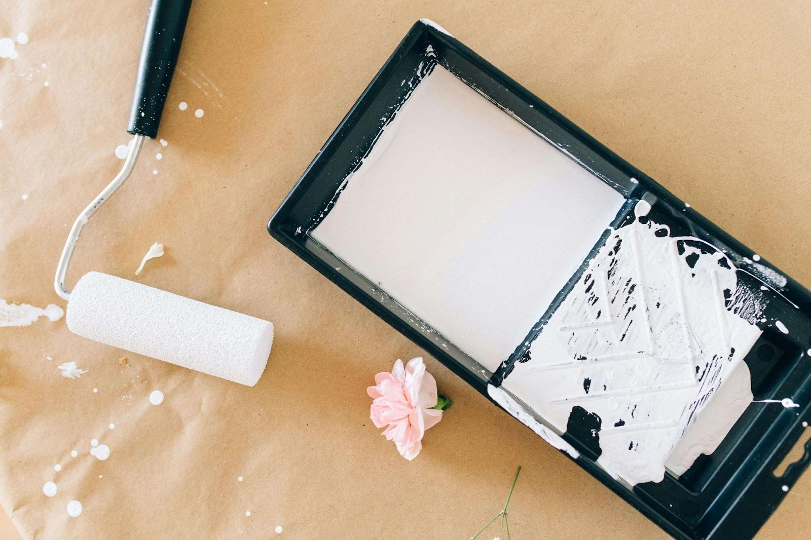 A box of paint, a paint roller, and a paint brush, symbolizing professional painting services for home improvement.