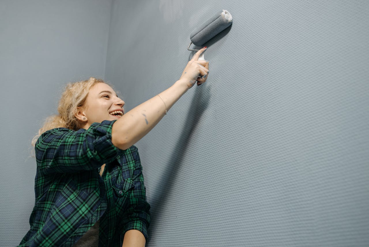 A woman expertly paints a wall with a roller, showing her skills at Athena Best Painting Services.