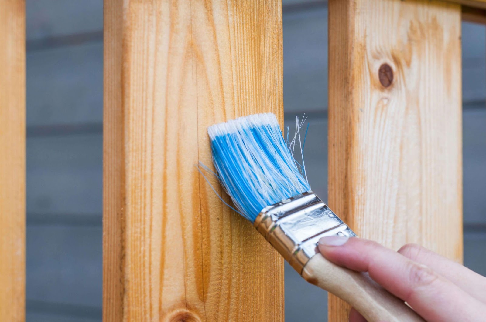 A person applies a faux finish to a wooden fence using a brush, showing creativity and workmanship in outdoor decor.