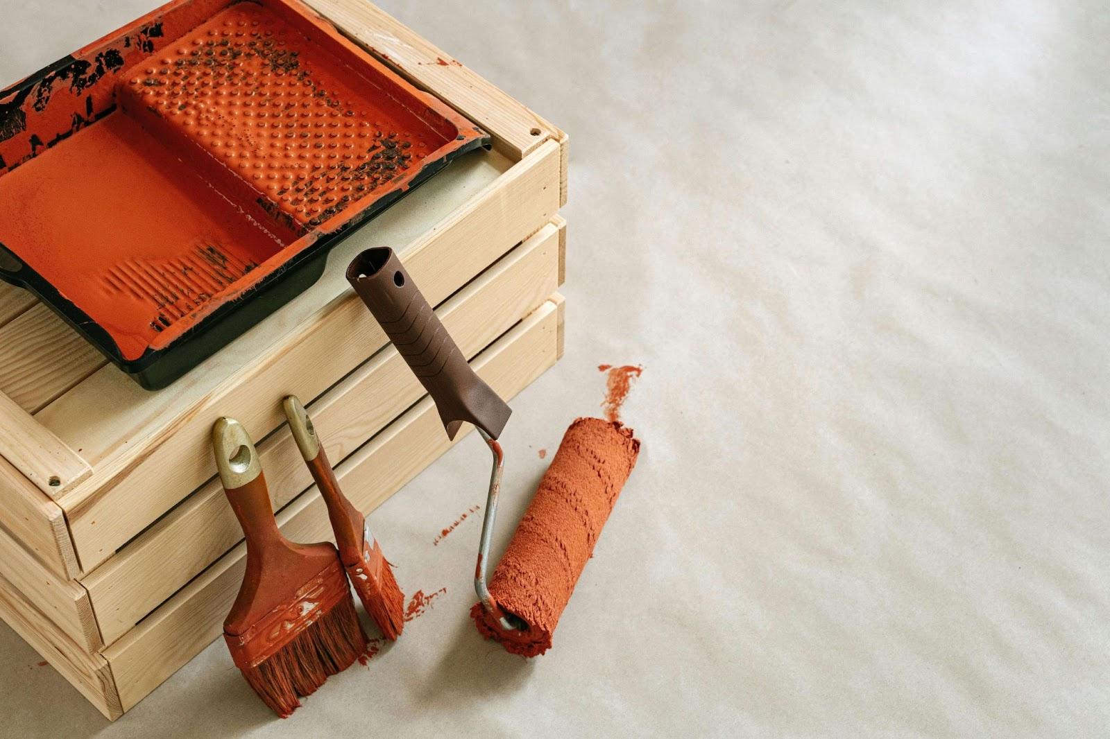 A wooden box containing eco-friendly paints, brushes, and a paint roller, showing a creative workspace.