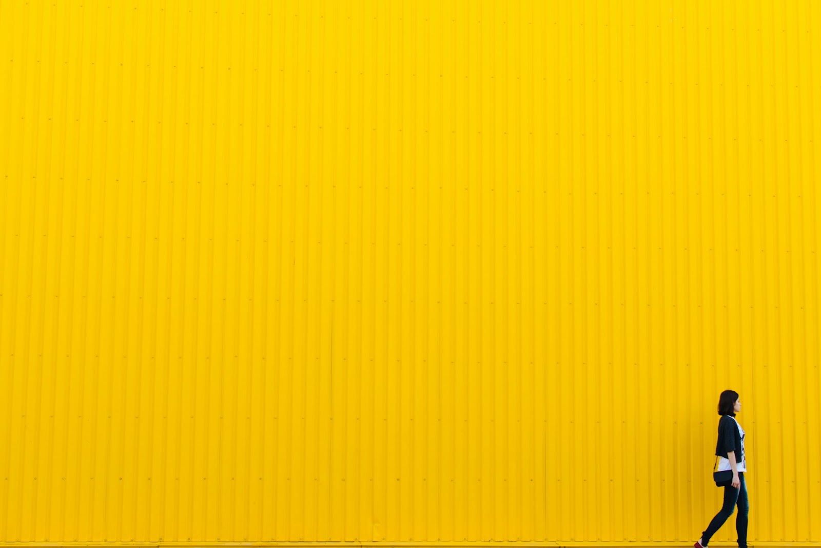 A person walks in front of a bright yellow wall, showing a lively urban scene in Singapore.