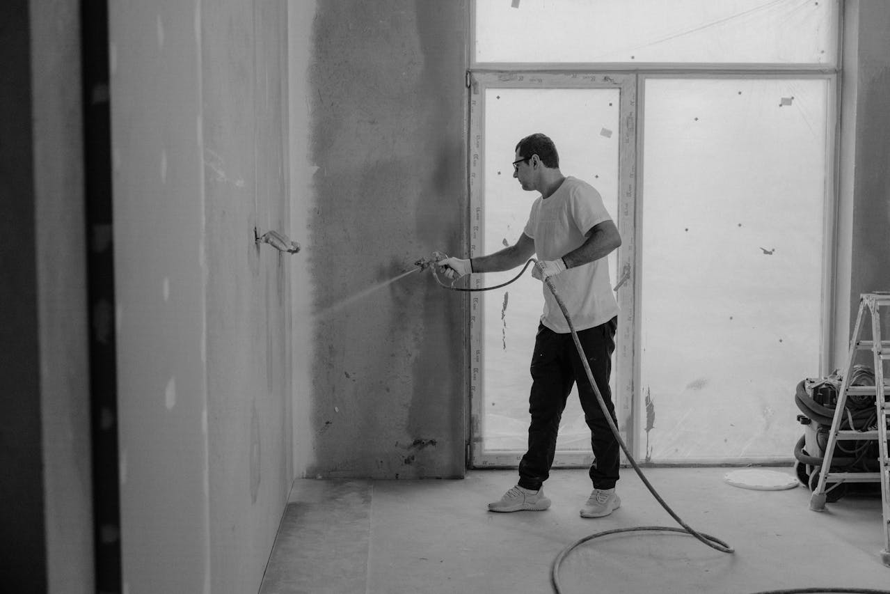 A man uses a hose to paint a room, showing the expertise of Athena Best Painting Services.