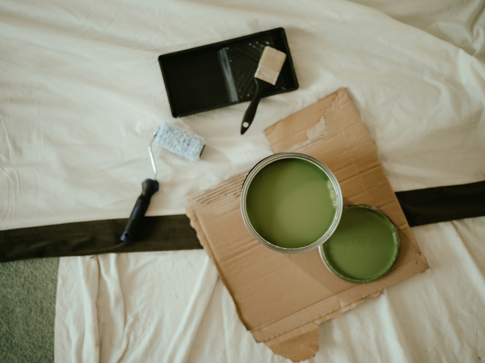 A paint can, brush, and roller arranged on a bed, symbolizing preparation for a painting project by Athena Best Painting Services.